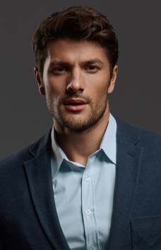 Young beautiful confident european businessman. Front view of bearded man with dark hair clothing formal suit and looking at camera. Isolated on dark gray background. Studio shoot